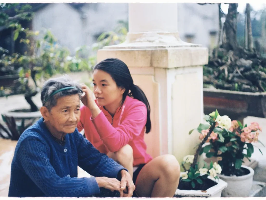 Cháu gái ngồi cạnh chải tóc cho bà ngoài sân nhà
