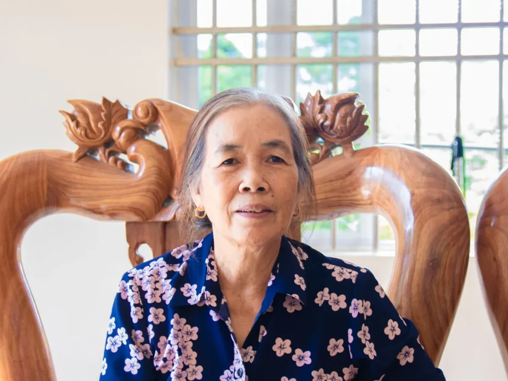 Cụ bà ngồi trên ghế gỗ trong phòng khách tại nhà